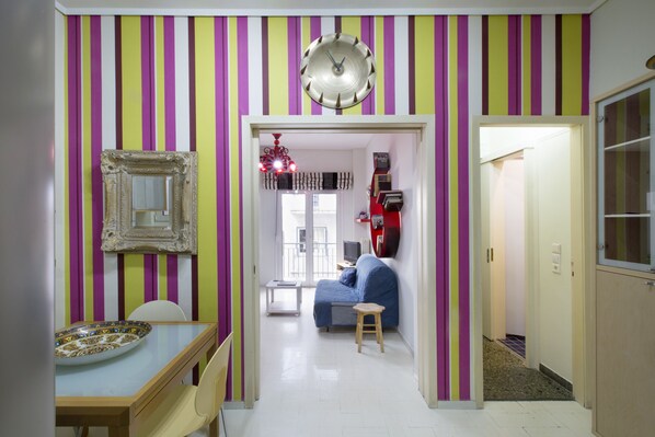 A hallway with a dining area, a blue sofa, and a clock on the wall.