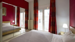 Ett hotellrum med en stor säng, ett nattduksbord med en lampa, en spegel och utsikt över omgivningarna genom en skjutdörr av glas.