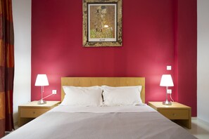 A hotel room with a large bed, two bedside tables, and a red wall.