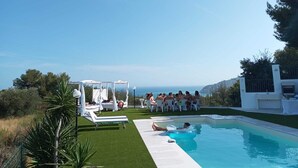 A poolside area with lounge chairs, a small pool, and a group of people gathered near a white gazebo.
