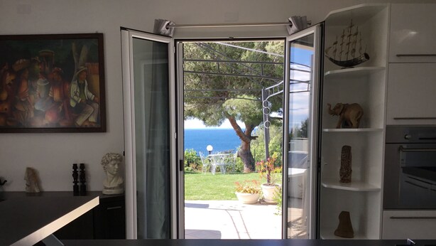 A kitchen with a view of a garden and the sea.