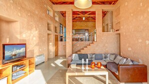 Uma sala de estar ampla, com teto alto, uma escada para um andar superior e uma televisão em uma prateleira de madeira.