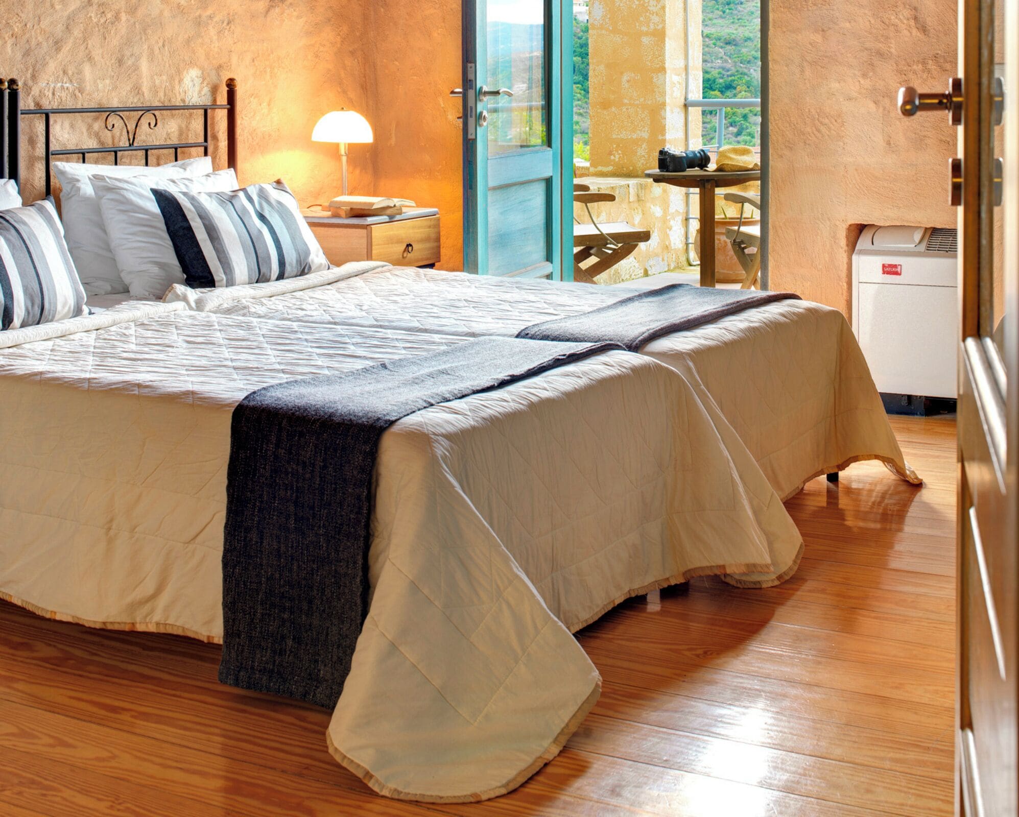 A large bed with a quilt, a bedside lamp, and a view of the outdoors through a door.