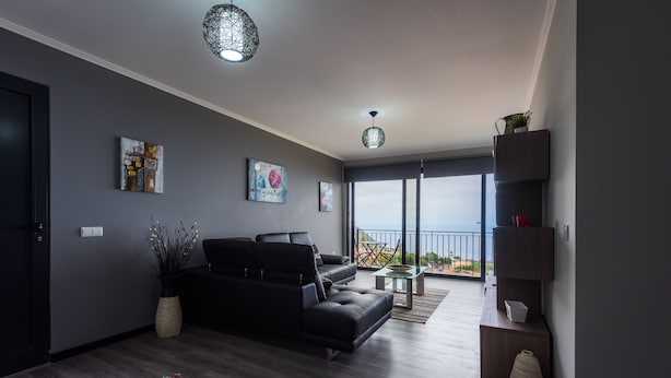 A modern living room with a black sofa, a glass coffee table, and artwork on the walls. - Super OCEAN VIEWS - Modern 2 Bed Apartment Stylishly Furnished (Arco da Calheta)