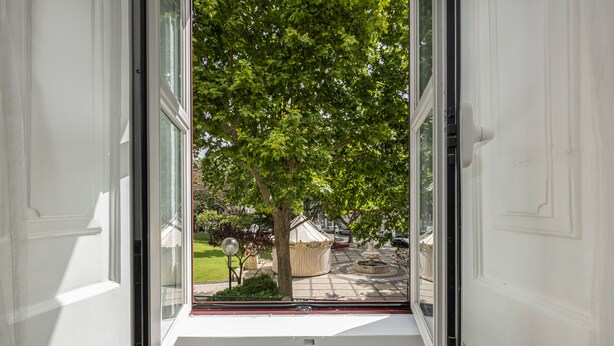 A view from a room with a large window, looking out to a tree-lined street and a gazebo. - Charming apartment (Cascais)