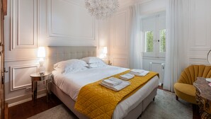 A hotel room with a large bed, two bedside tables, a yellow quilt, and a modern chandelier. - Charming apartment (Cascais)