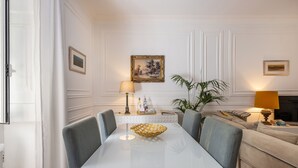 A dining area with a white table, chairs, and a decorative bowl. There is a sofa and a lamp in the background. - Charming apartment (Cascais)