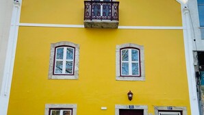 A yellow building with a dark brown door, a balcony with ornate railings, and a sign indicating a business. - Charming apartment (Cascais)