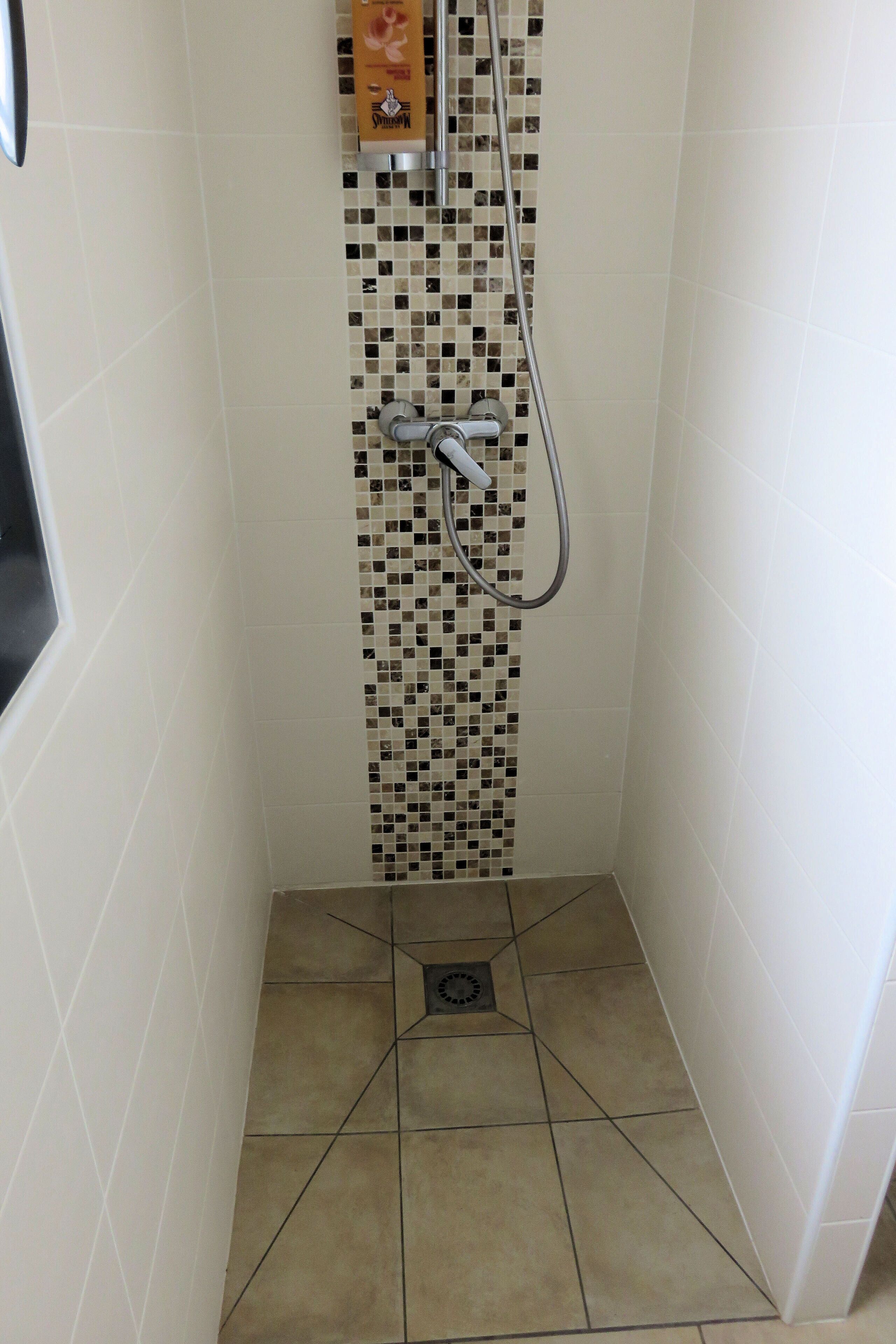 A small, tiled shower area with a mosaic tile design on the wall, a showerhead, and a drain.