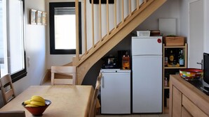 Eine kleine Küche mit Esstisch, Kühlschrank und einer Holztreppe.