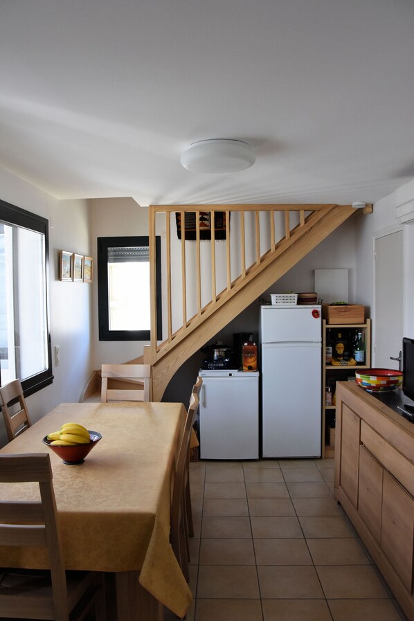 Cocina compacta con mesa de comedor, refrigerador y una escalera de madera.