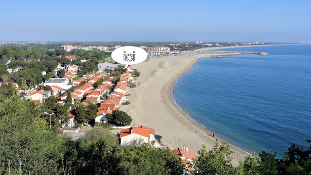 Eine Küstenstadt mit Strand, Häusern mit roten Dächern und blauem Himmel.