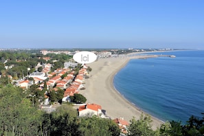 A coastal town with a beach, houses with red roofs, and a clear blue sky.