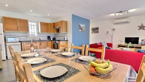 A modern kitchen with wooden cabinets, a dining table set for four, and a red sofa in the living area. - Beautiful villa 6 pers  3 rooms fenced with private pool in Vallon Pont d'Arc (Vallon-Pont-D'arc)