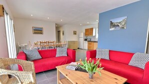 A living room with a red sofa set, a wooden coffee table, and a wicker chair. There is a dining table with chairs in the background. - Beautiful villa 6 pers  3 rooms fenced with private pool in Vallon Pont d'Arc (Vallon-Pont-D'arc)