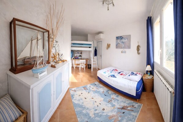 A bedroom with a bed, a desk, and a chair. There is a window with curtains, a radiator, and a wall-mounted shelf with decorative items. - House / Villa - MONTAUROUX (Montauroux)