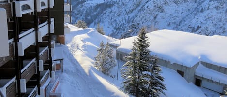 A snow-covered mountain with a ski slope, a building with balconies, and a few trees.