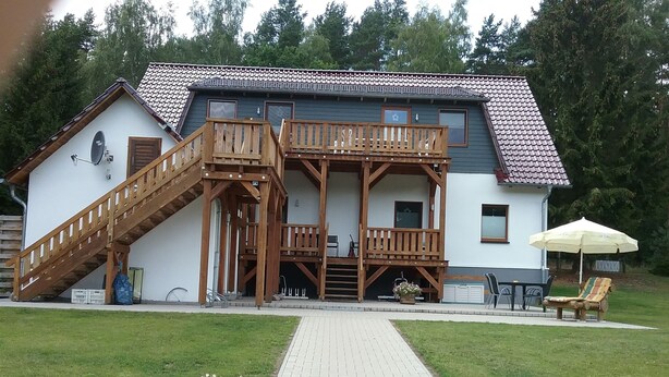 A two-story house with a wooden deck, a staircase, and a covered outdoor seating area. - Welcome to our apartments of Villa Wald-Eck (Apartment 2)  (Ückeritz)
