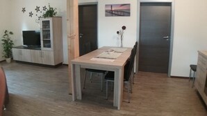 A dining area with a table, chairs, and a TV on a cabinet. - Welcome to our apartments of Villa Wald-Eck (Apartment 2)  (Ückeritz)