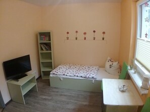 Une petite pièce avec un lit, un téléviseur posé sur un meuble, une bibliothèque et une fenêtre donnant sur un paysage agréable.