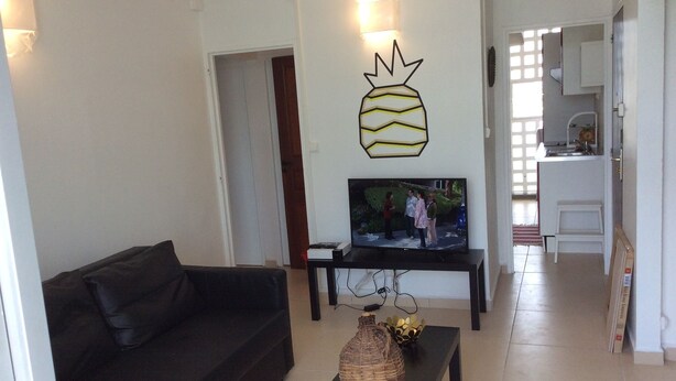 Un salon avec un canapé noir, un téléviseur et une décoration murale représentant un ananas.