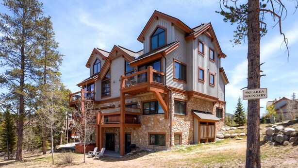 A multi-story lodge with a stone facade, wooden balconies, and a ski area boundary sign. - Super Ski Pad - True Ski-In/Ski-Out Retreat. Private Hot Tub. Walk to Adventure (Breckenridge)