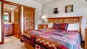 A bedroom with a wooden headboard, a colorful quilt, a bedside table with a lamp, and a mirror. - Super Ski Pad - True Ski-In/Ski-Out Retreat. Private Hot Tub. Walk to Adventure (Breckenridge)