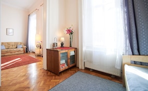 A well-lit living room with a sofa, a wooden cabinet, a radiator, and a window with curtains.