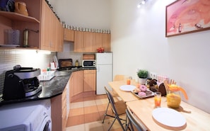 A compact kitchen with wooden cabinets, a microwave, a refrigerator, and a dining area with a table set for breakfast.