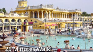 A large outdoor swimming pool with people enjoying the water, surrounded by a yellow building with classical architecture.