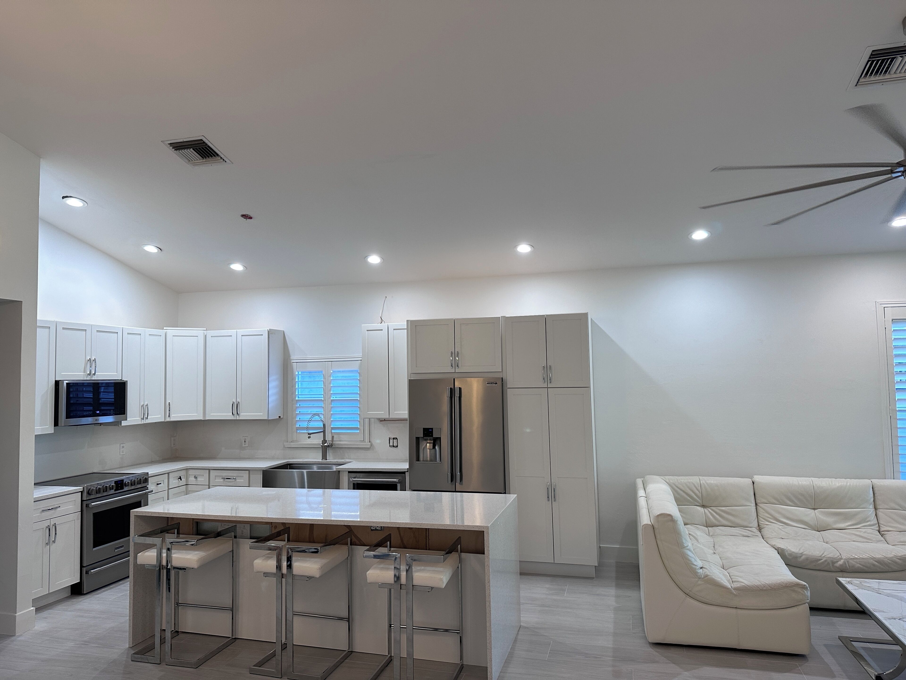 A modern kitchen with white cabinetry, a central island with bar stools, a built-in oven, and a refrigerator.