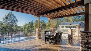 A covered outdoor deck with a wooden table and chairs, stone pillars, and a view of a house and forest. - Gorgeous Colorado Farmhouse Getaway in Forest, yet 10 min from town: NO EVENTS (Colorado Springs)