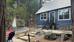 A blue building with a stone foundation, a staircase, and a red chair outside. - Adorable Mountain Getaway (Shaver Lake)