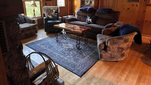 A cozy living room with a stone fireplace, wooden walls, and a large window. - Adorable Mountain Getaway (Shaver Lake)