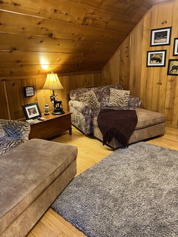 A cozy room with a wooden ceiling, a sofa with zebra print, a small table with a lamp, and framed pictures on the wall. - Adorable Mountain Getaway (Shaver Lake)