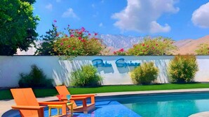 A pool area with lounge chairs, a towel, and bottles, with a sign reading "Blye Springs" in the background. - Best Views! Golden Girls themed House. Pool and Spa! (Palm Springs)