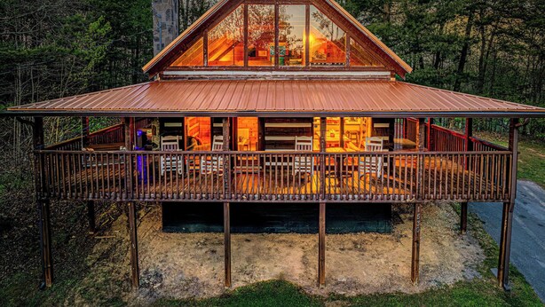 A cabin with a large glass front, wooden deck, and a stone chimney. - Hot tub. Views. Multicade & Foosball! (Sevierville)