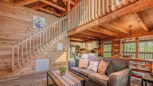 A wooden cabin interior with a staircase, a living room with a sofa and a table, and a kitchen area. - Hot tub. Views. Multicade & Foosball! (Sevierville)