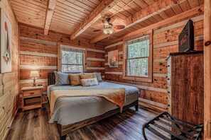 Une chambre dans une cabane en bois, comprenant un lit, une table de chevet, une commode et un ventilateur de plafond.