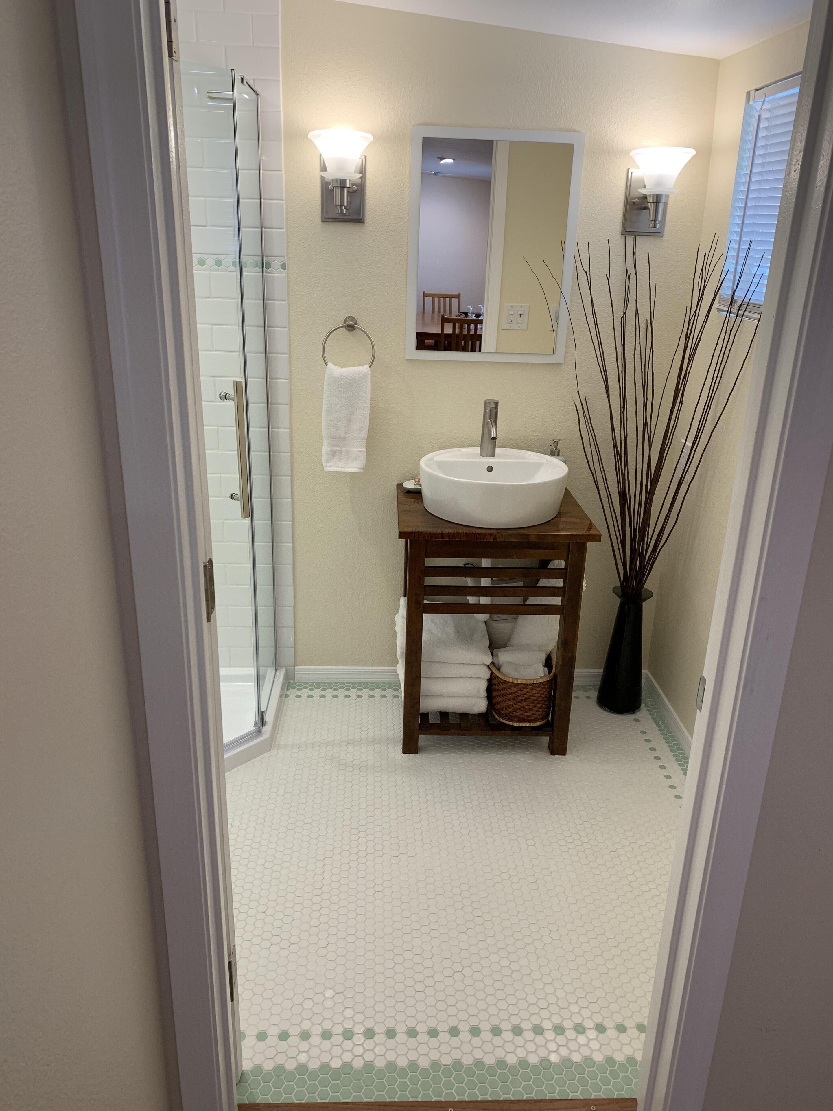 A bathroom with a glass shower door, a white sink, a wooden vanity, and a mirror above the sink.