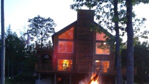 Een chalet met een vuurkuil ervoor, omringd door rotsen en bomen.