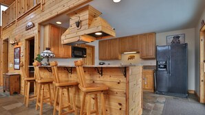 Een landelijke houten keuken met een bar, houten krukken en een koelkast.