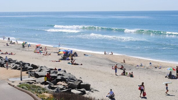 A beach with people sunbathing and swimming, a rocky shoreline, and waves crashing onto the shore. - Relax in Style in Carlsbad's Best Location (Carlsbad)