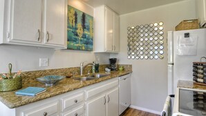 A kitchen with white cabinets, a granite countertop, a coffee maker, and a wall-mounted mirror. - Relax in Style in Carlsbad's Best Location (Carlsbad)