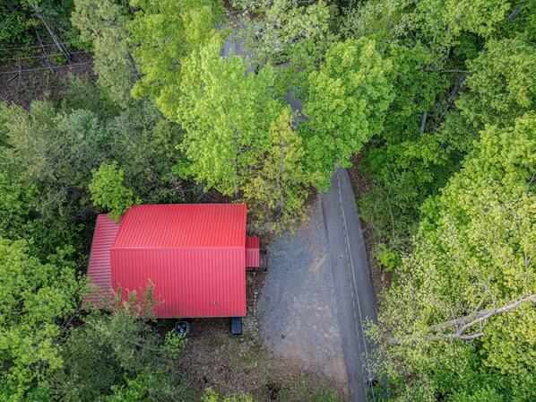 Un bâtiment rouge, avec une route pavée menant à l’entrée, entouré d’un feuillage verdoyant et dense.