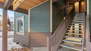 A wooden staircase leading to a house entrance with a porch and a snow-covered ground.