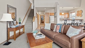 A living room with a brown leather sofa, a wooden coffee table, a side table with a lamp, and a staircase leading to another room.
