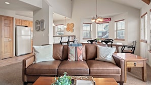 A spacious living room with a brown leather sofa, a wooden coffee table, and a dining area with a wooden table and chairs.