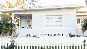 A white house with a sign that reads "SPREAD ALOHA" and a white picket fence. - The Family Beach House  (San Diego)
