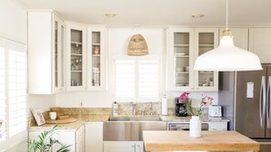 A modern kitchen with white cabinets, a stainless steel sink, a wooden countertop, and a hanging pendant light. - The Family Beach House  (San Diego)